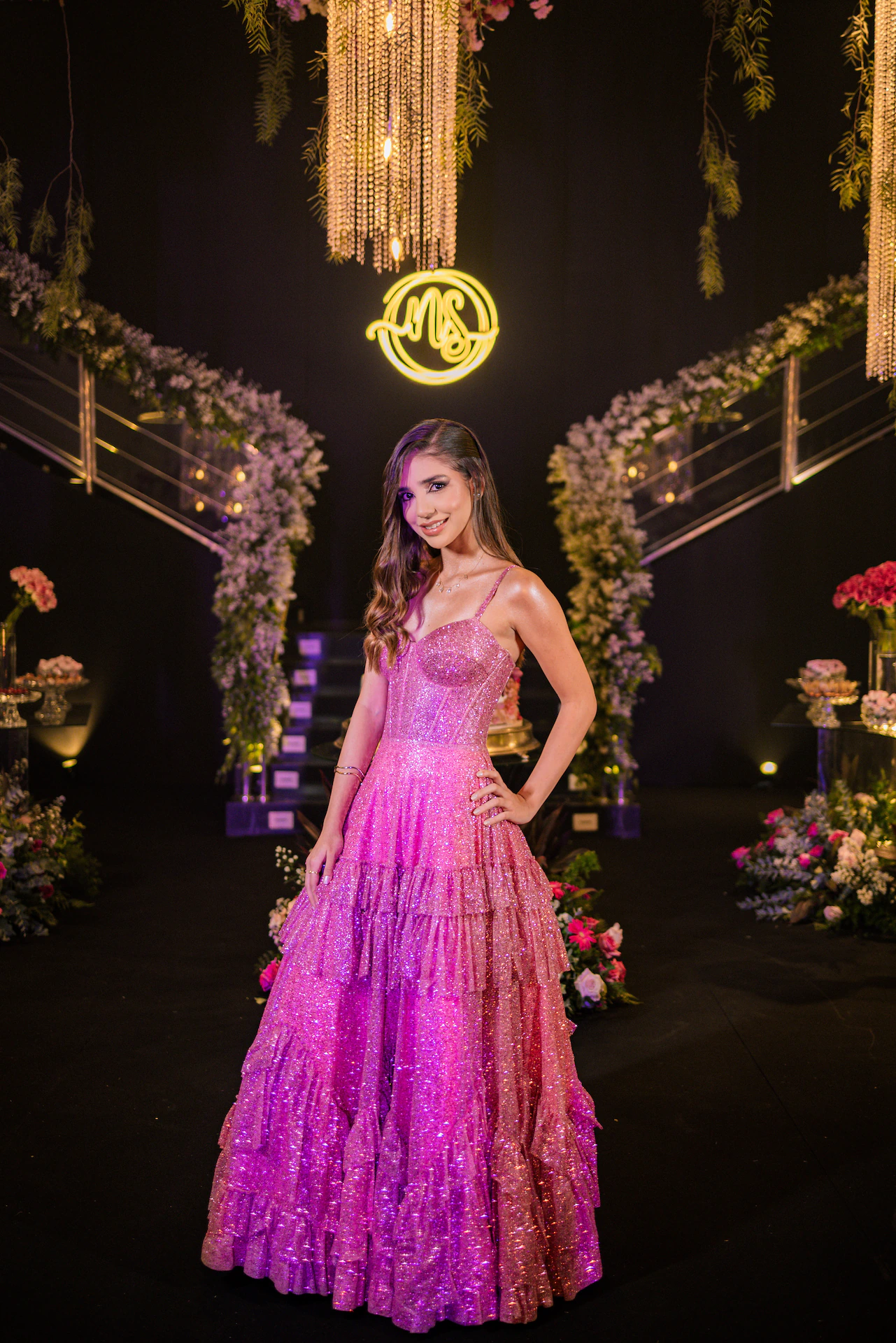 Debutante em vestido rosa diante do arco de flores iluminado na festa de 15 anos em Goiânia