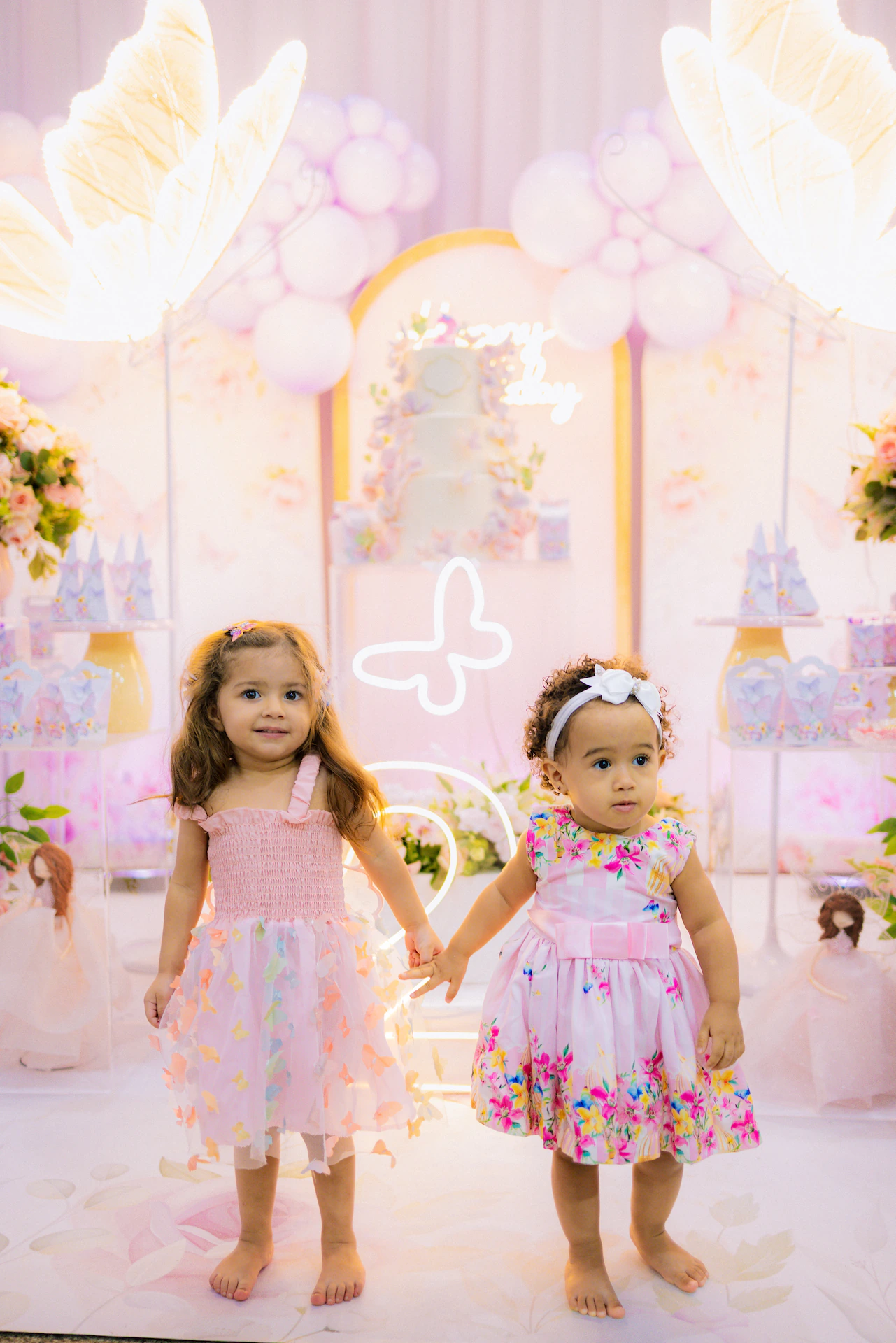 Duas meninas de mãos dadas em frente à decoração de festa infantil com balões
