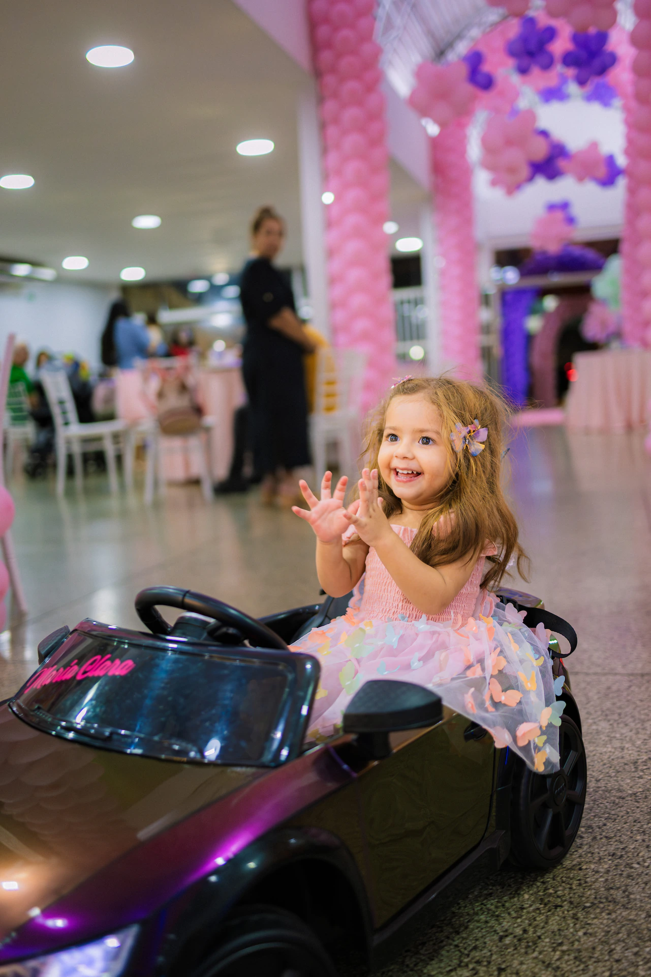 Menina acenando sentada em um carrinho elétrico no salão da festa infantil