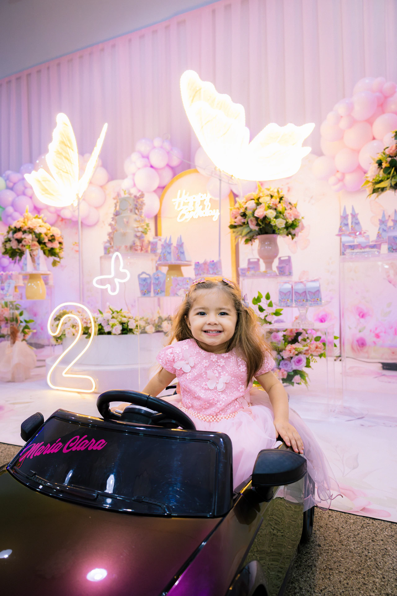 Menina no carrinho elétrico ao lado do número 2 na decoração de aniversário infantil em Goiânia