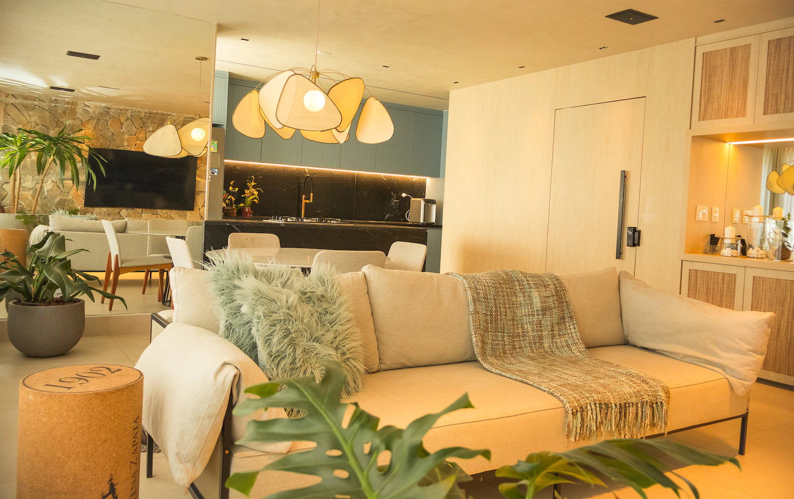 Sala de estar iluminada com luz quente, sofá claro e luminárias pendentes