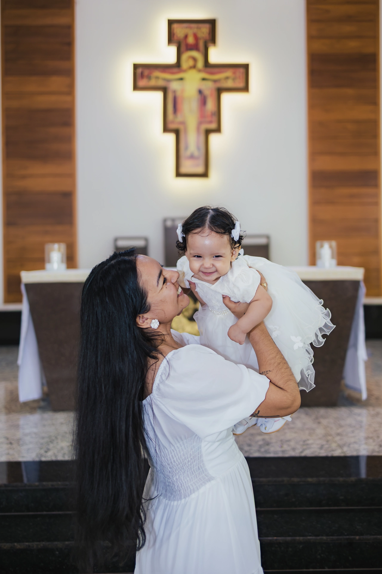 Mãe erguendo a bebê e sorrindo em frente ao altar da igreja