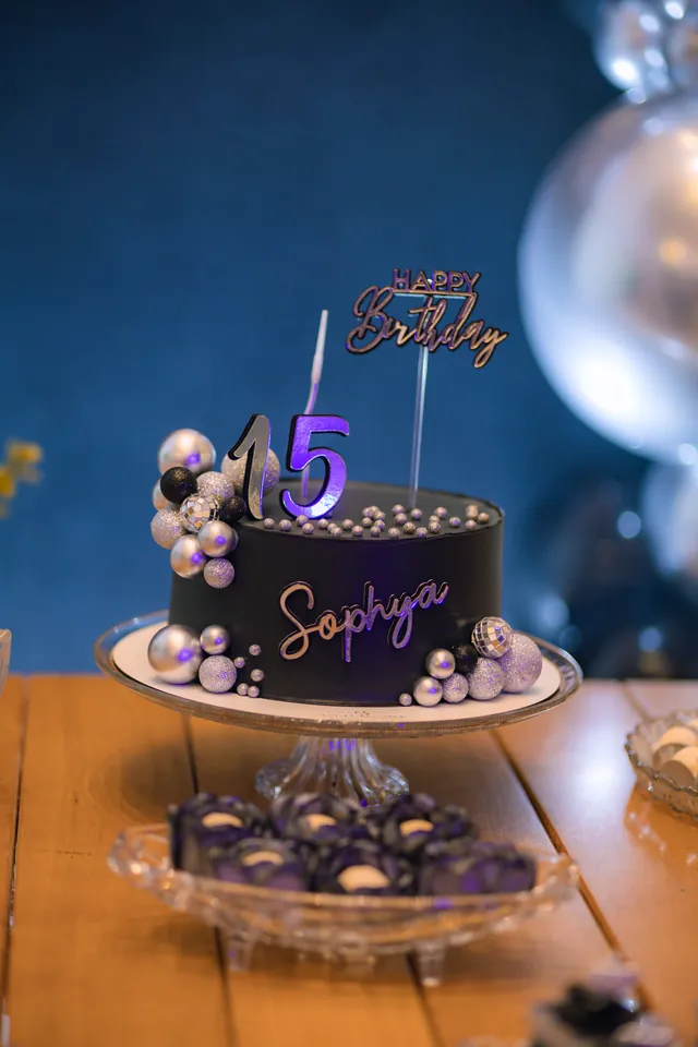 Bolo preto de 15 anos com o nome Sophya escrito em prata e o número 15 no topo