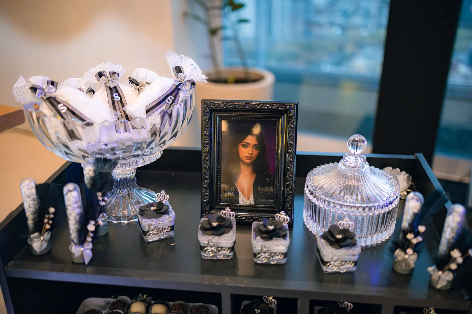 Aparador com bomboniere de cristal, doces com laço preto e retrato emoldurado da Sophya