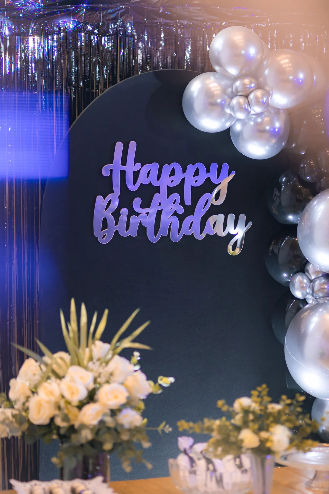 Painel escuro com Happy Birthday em acrílico prata, rosas brancas e balões metalizados