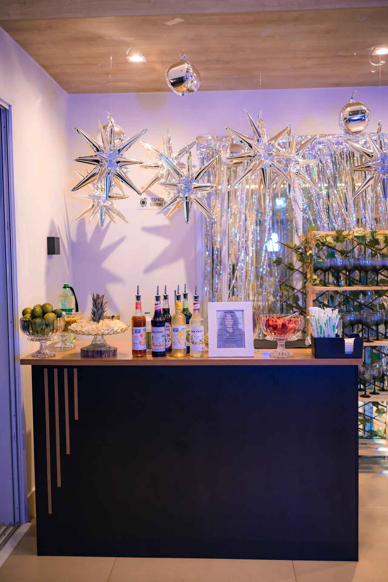 Bar de drinks com cortina metalizada prata e estrelas de balão penduradas no teto
