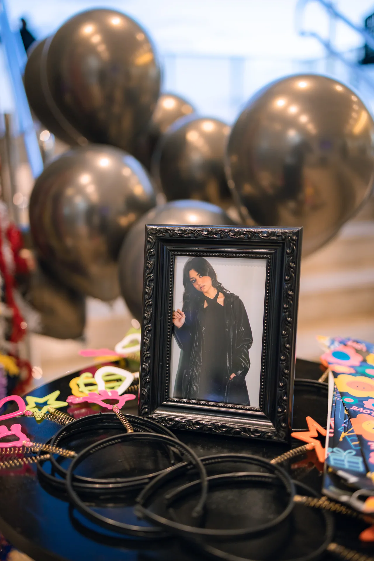 Retrato da Sophya em moldura preta entre balões cromados e pulseiras pretas