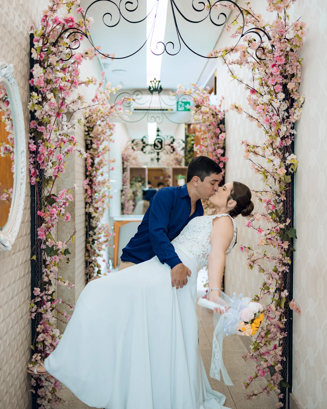 Os noivos se beijando sob um arco florido no corredor do cartório em Goiânia