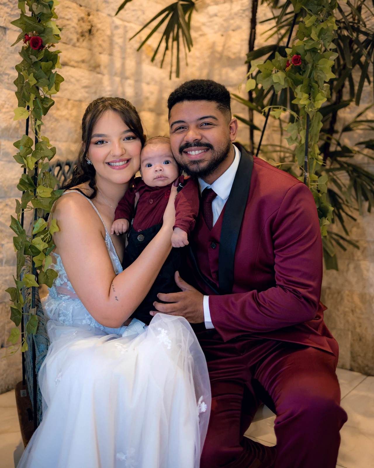 Os noivos agachados segurando o bebê e sorrindo