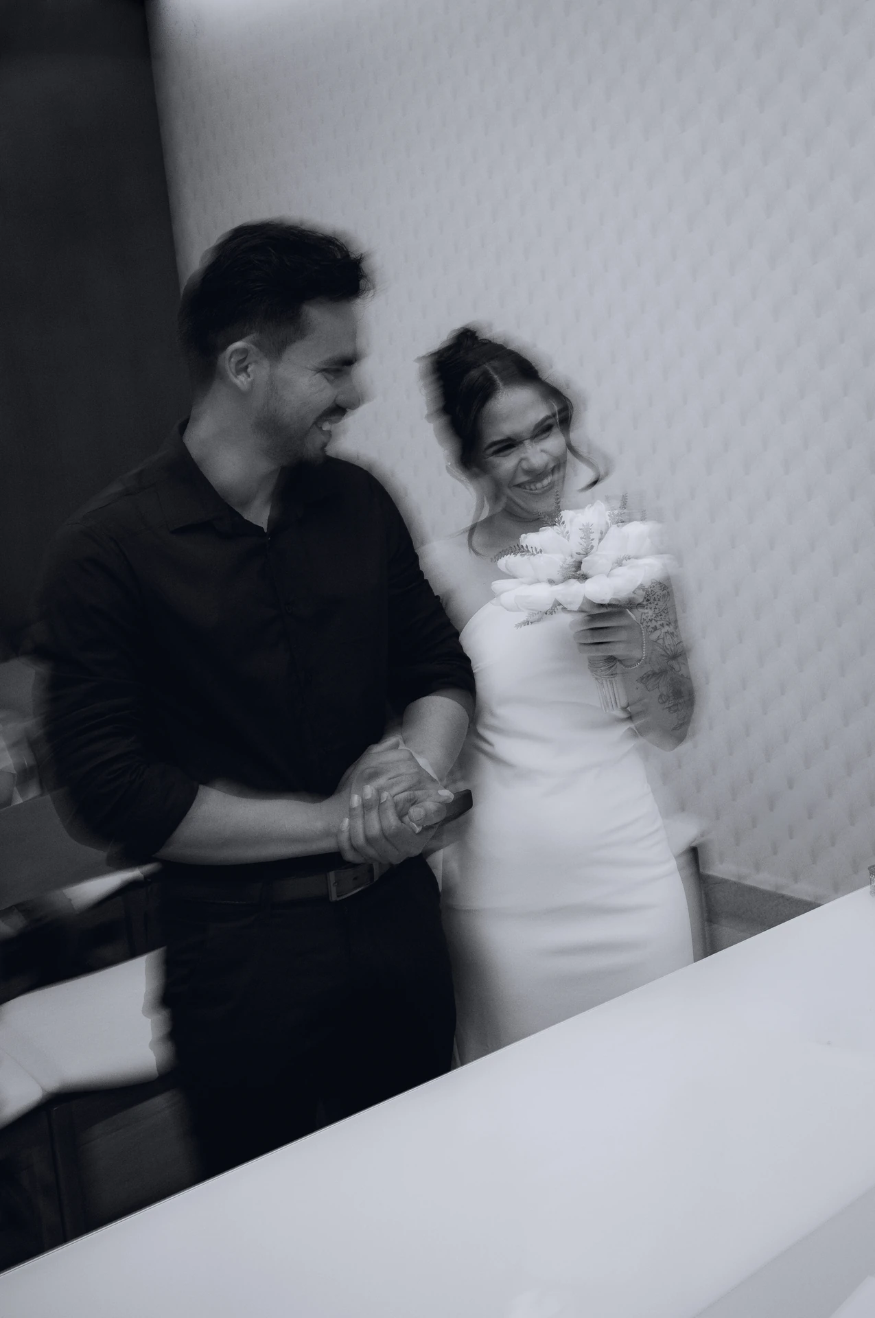 José e Alice rindo juntos, de mãos dadas, em preto e branco, em foto com movimento