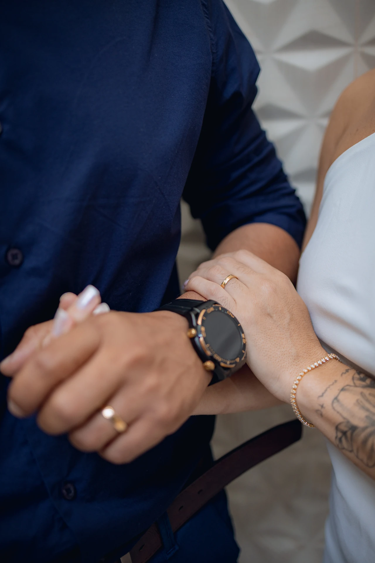 Detalhe das mãos dos noivos com as alianças, ela com pulseira e ele com relógio