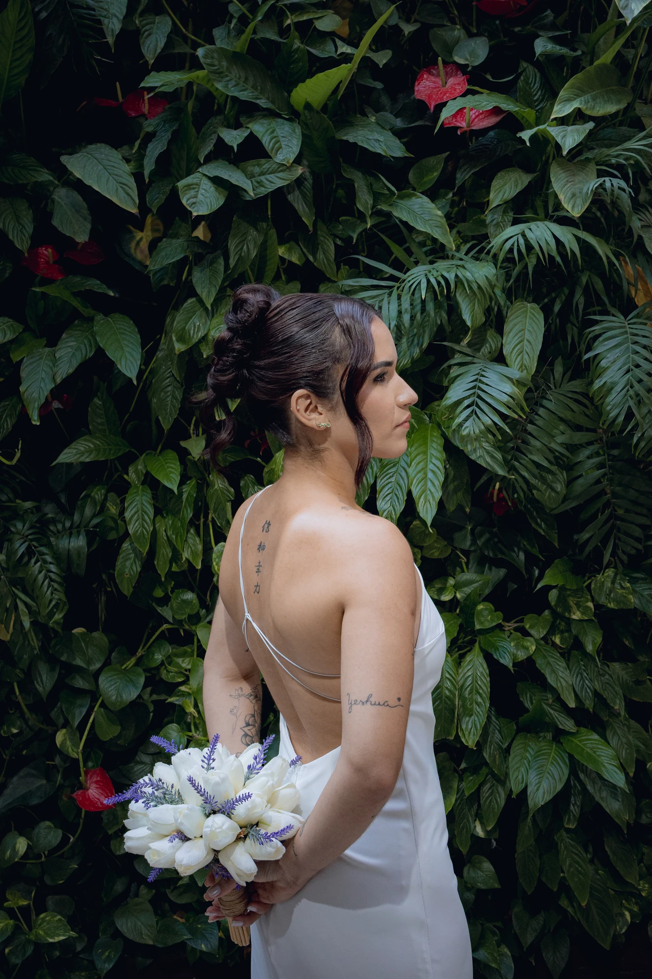 Alice de costas diante da parede de folhagens, segurando o buquê de flores brancas