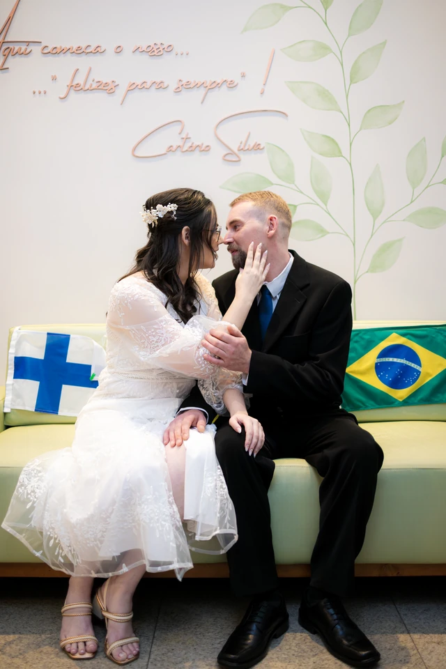 Noivos sentados após o casamento civil em Goiânia com bandeiras do Brasil e da Finlândia