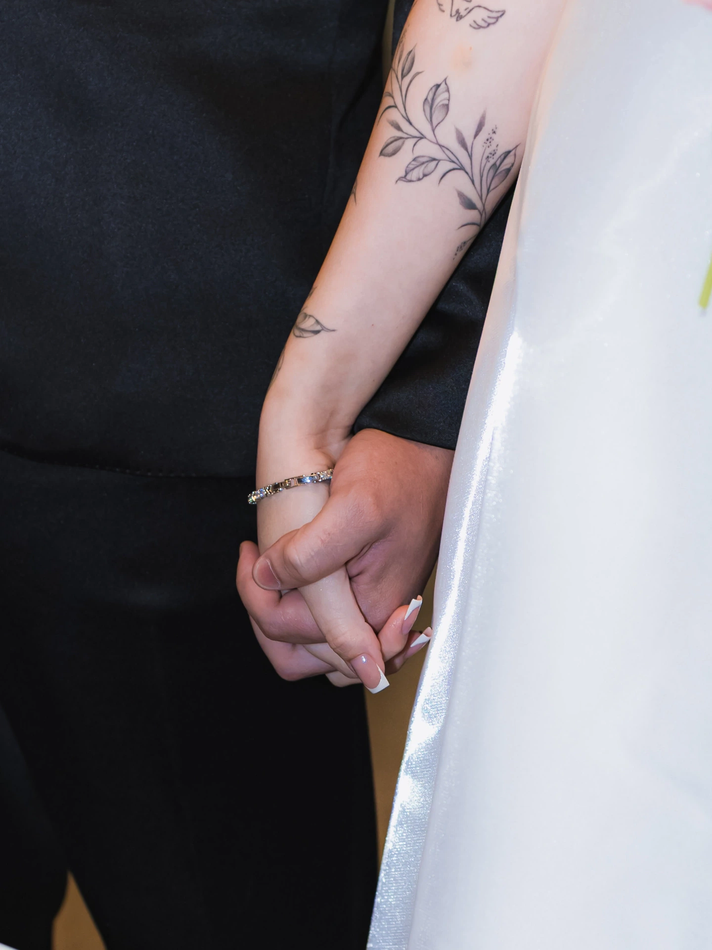 Detalhe das mãos dadas dos noivos, com a tatuagem no braço da noiva