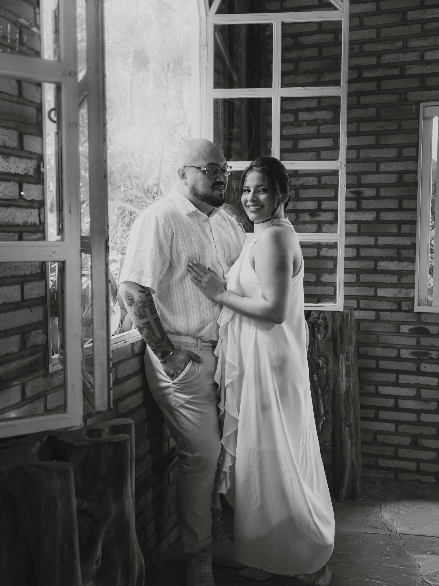 Foto em preto e branco de Jessica e Alex abraçados perto da janela
