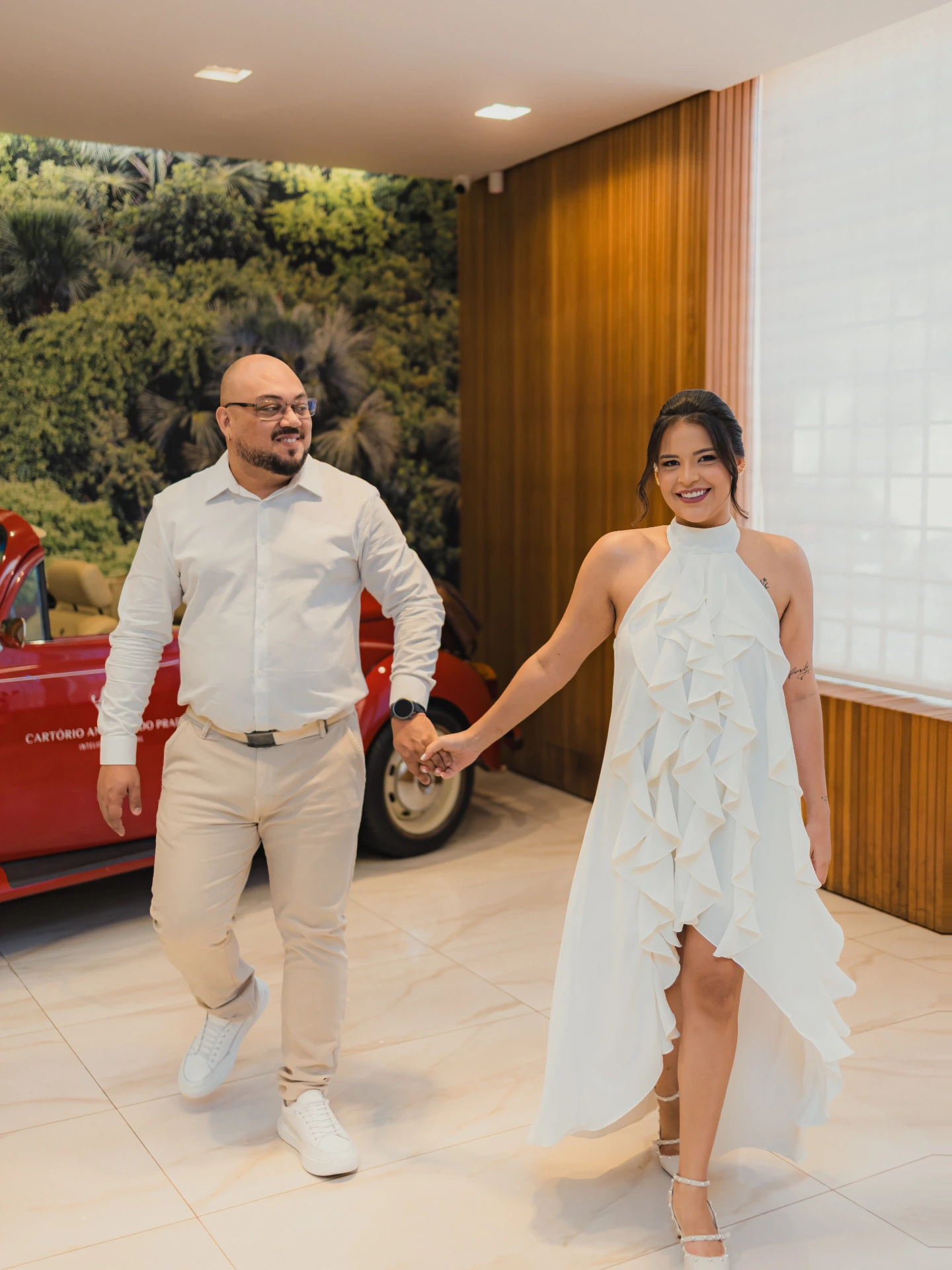 Jessica e Alex de mãos dadas caminhando, com um carro antigo vermelho ao fundo