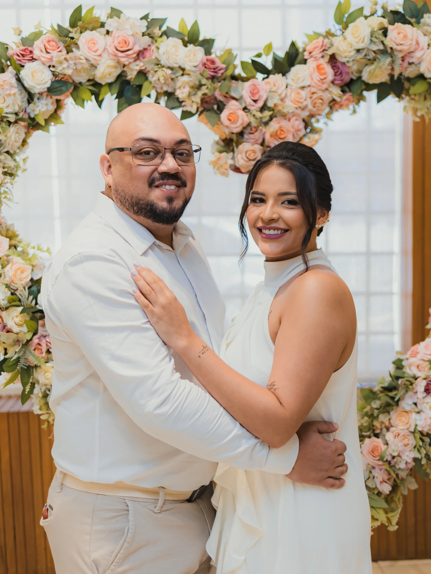 Os noivos abraçados e sorrindo sob o arco de flores