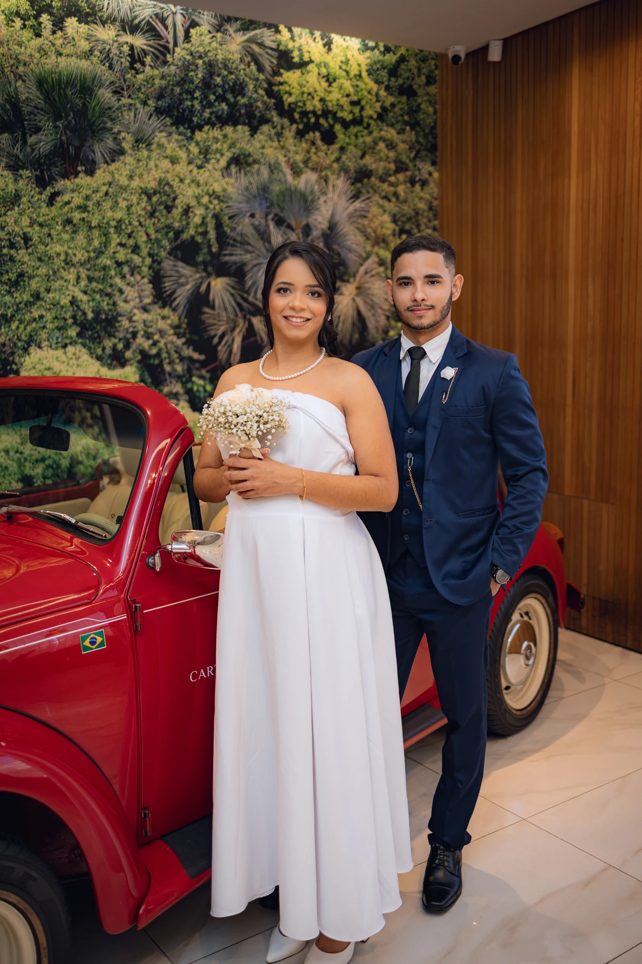 Jéssica e Thiago ao lado do carro antigo vermelho decorado do Cartório Antônio do Prado, em Goiânia