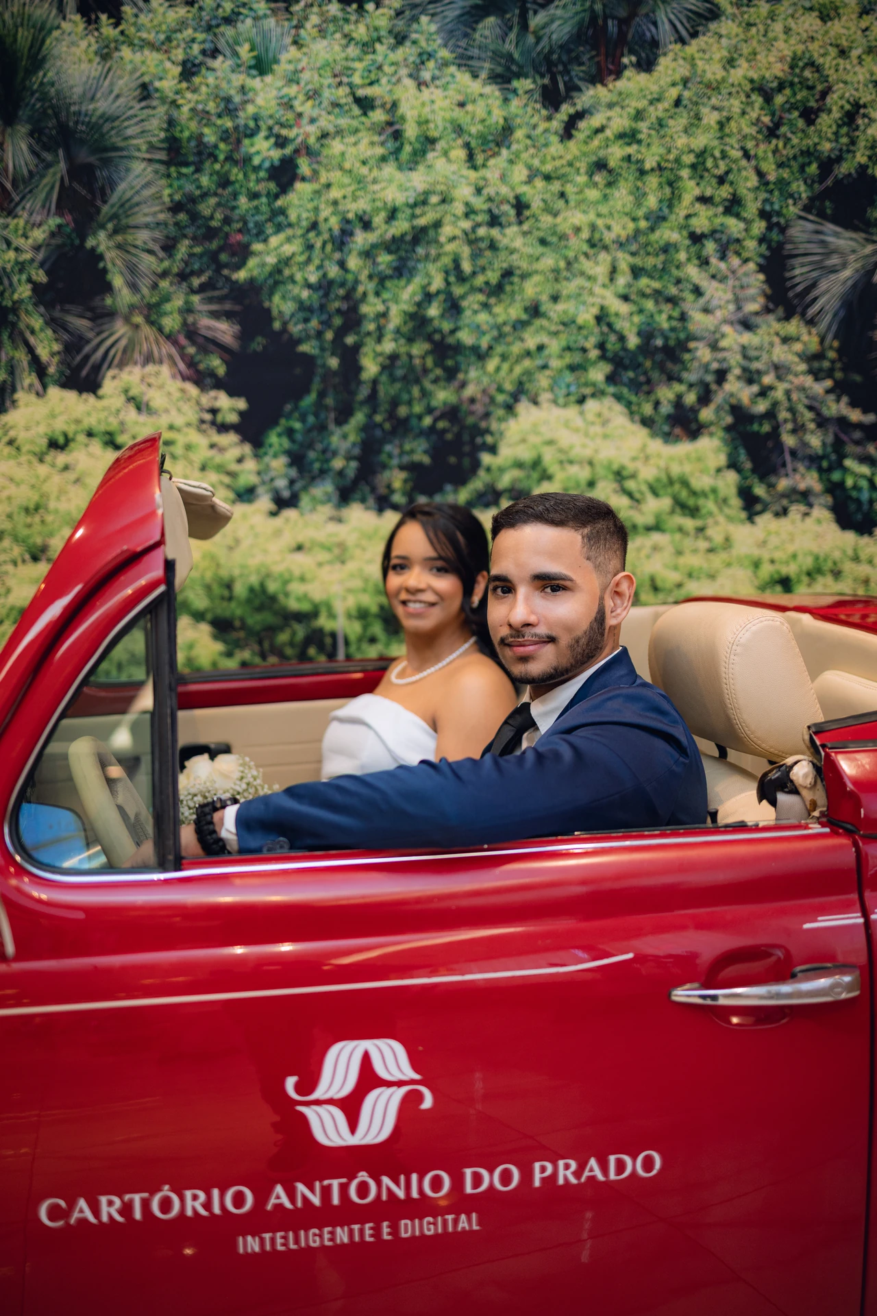 Jéssica e Thiago dentro do carro antigo vermelho, olhando para trás e sorrindo