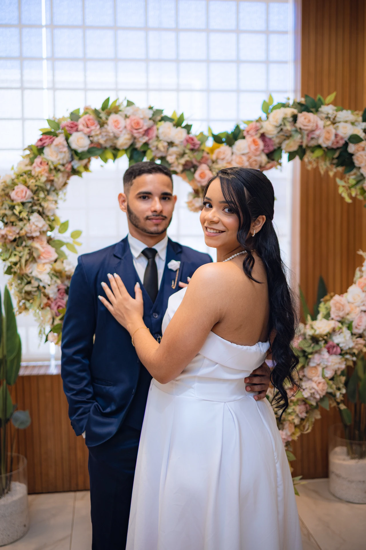 Jéssica e Thiago abraçados sob um arco de flores em formato de coração no Cartório Antônio do Prado