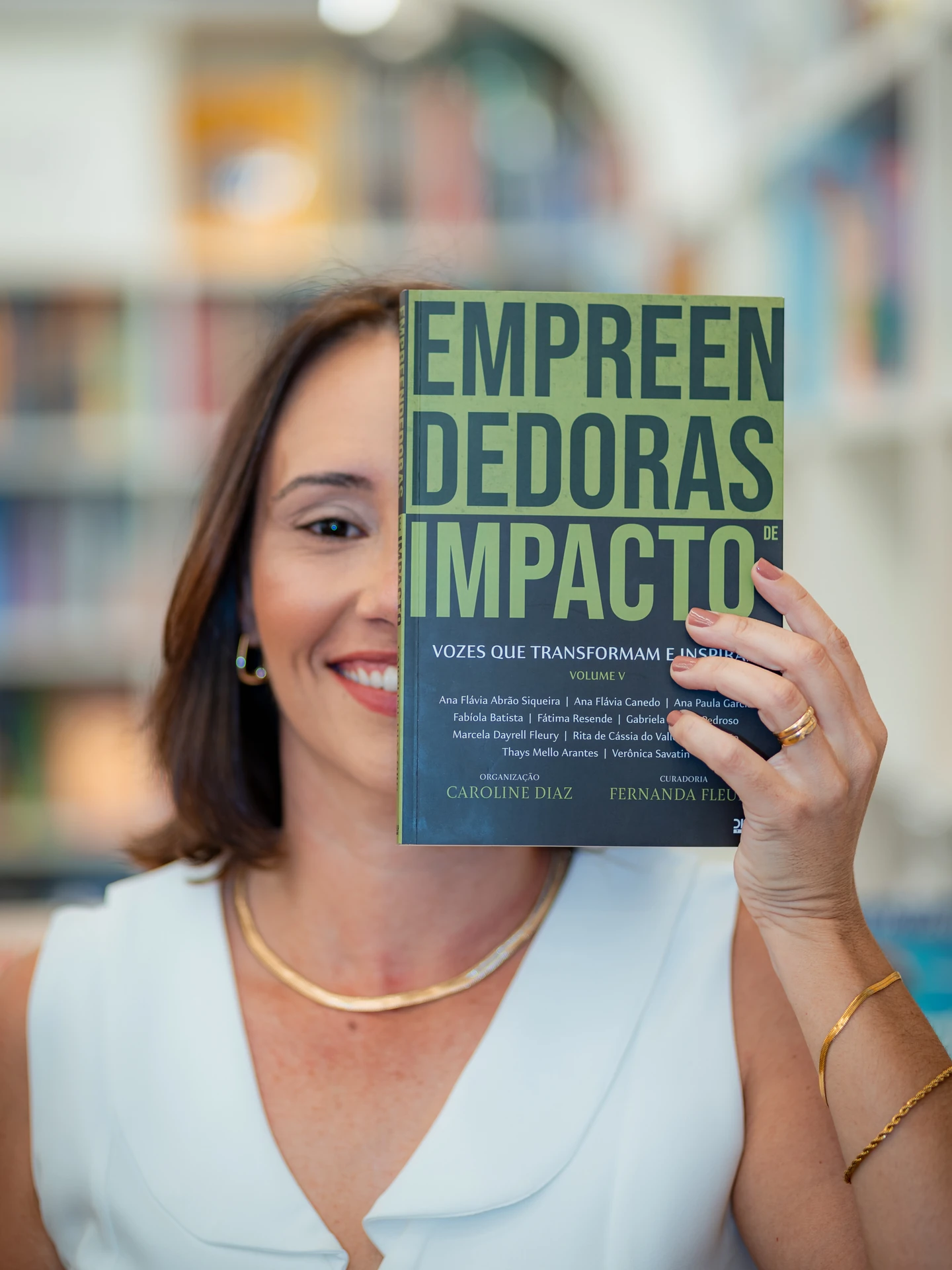 Autora sorrindo com o livro Empreendedoras de Impacto erguido diante do rosto, no lançamento em Goiânia