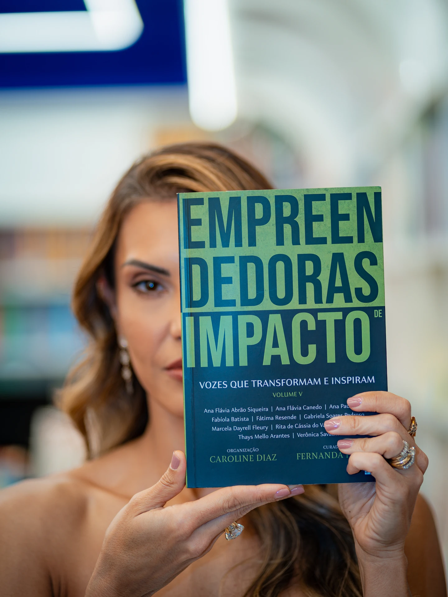 Autora segurando o livro Empreendedoras de Impacto com a capa virada para a câmera, em close