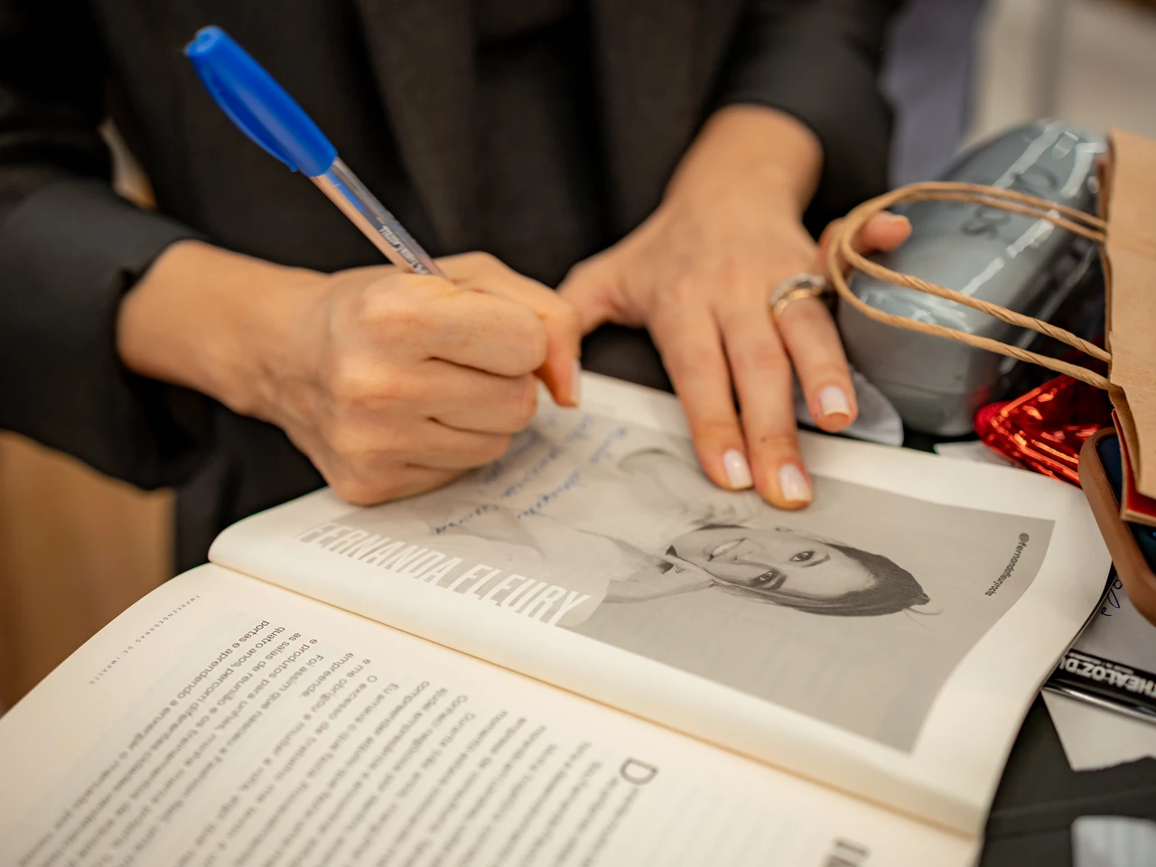 Mão assinando com caneta azul uma página do livro Empreendedoras de Impacto