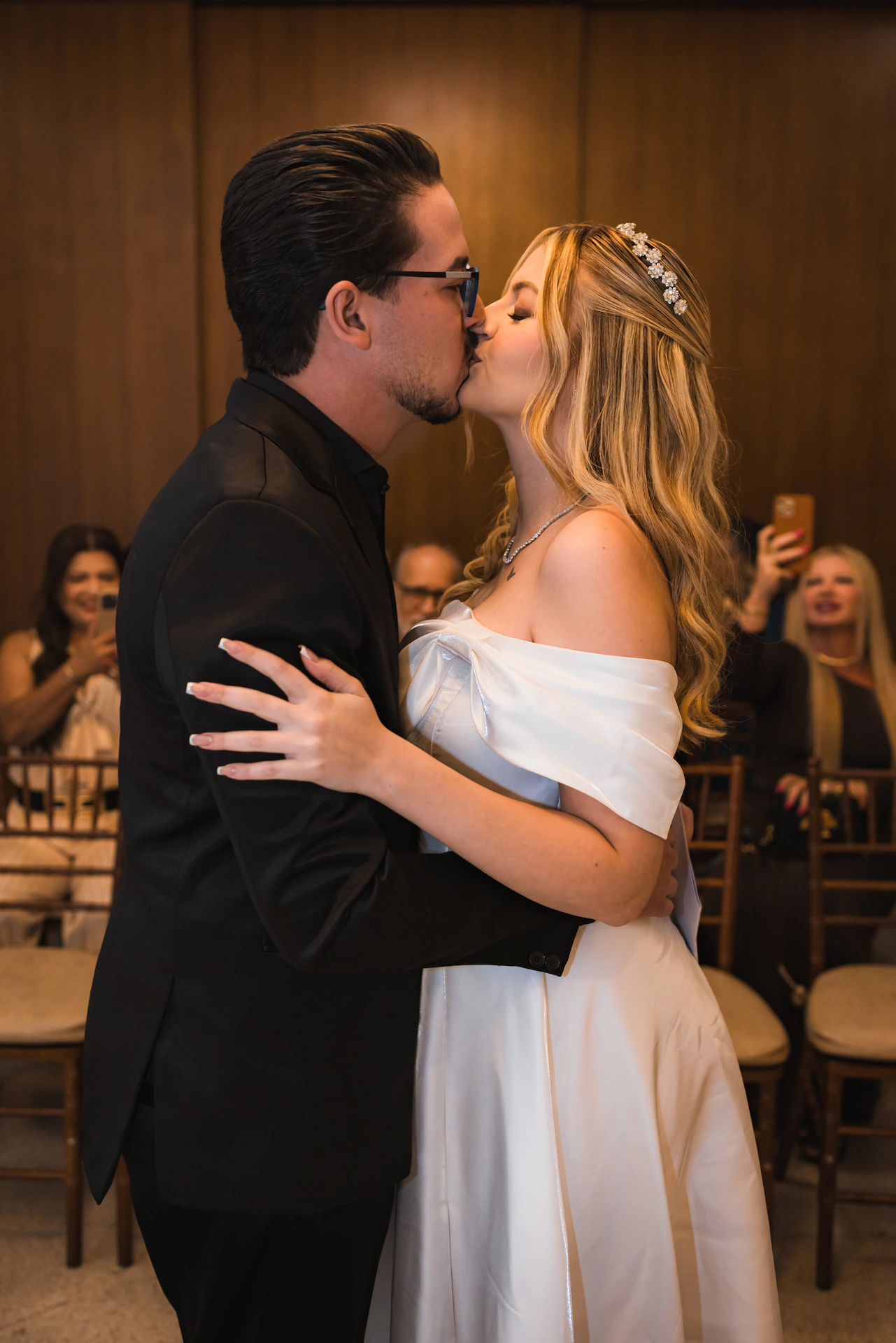 Noivos se beijando na cerimônia de casamento civil, com convidados ao fundo