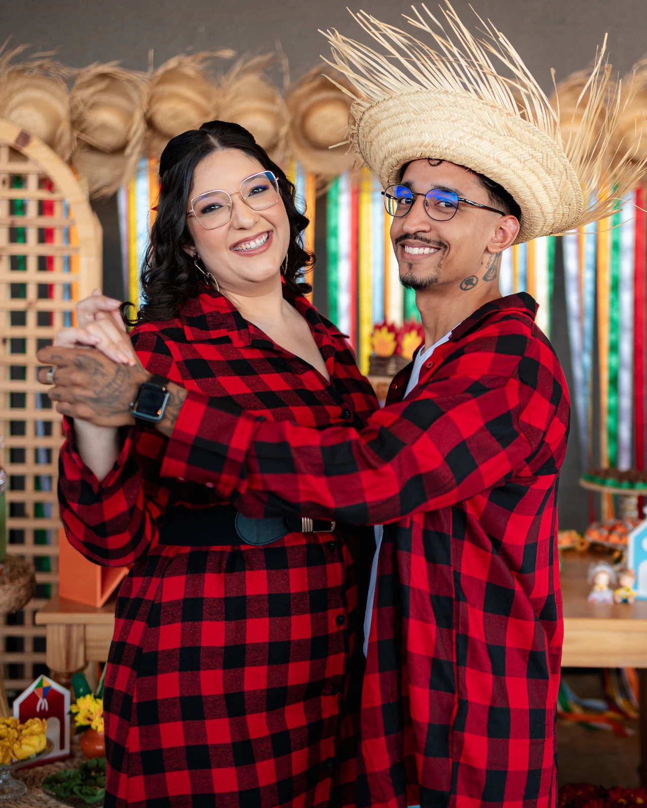 Casal de chapéu de palha e camisa xadrez dançando no cenário de festa junina