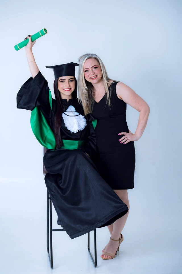 Formanda comemorando com o diploma erguido ao lado da mãe, ensaio de formatura em estúdio
