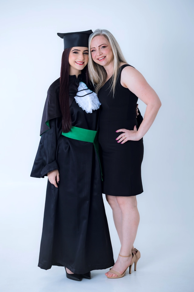 Formanda e mãe posando juntas em fundo neutro de estúdio