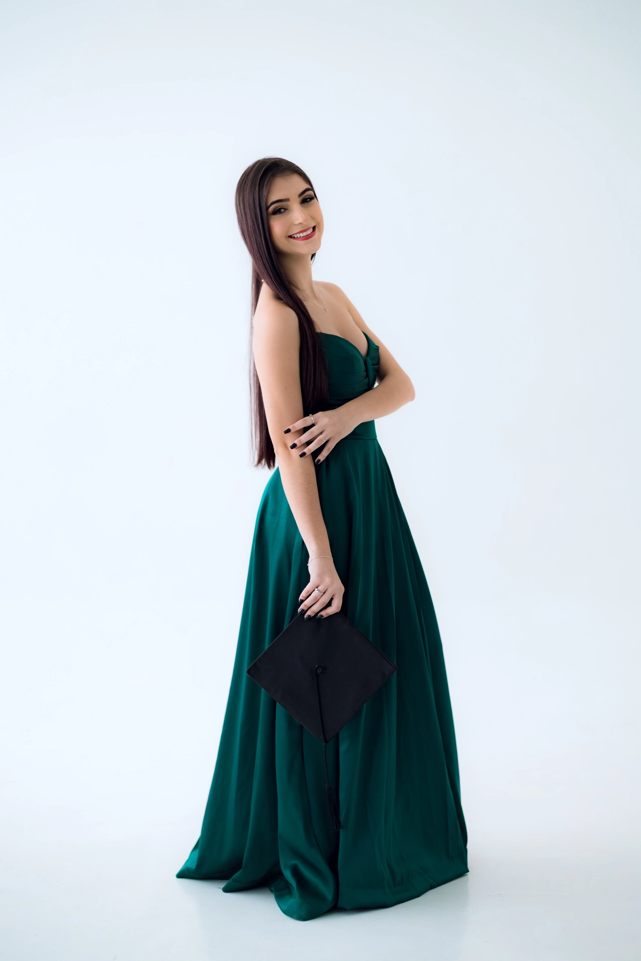 Formanda de vestido verde segurando o capelo na mão, retrato solo