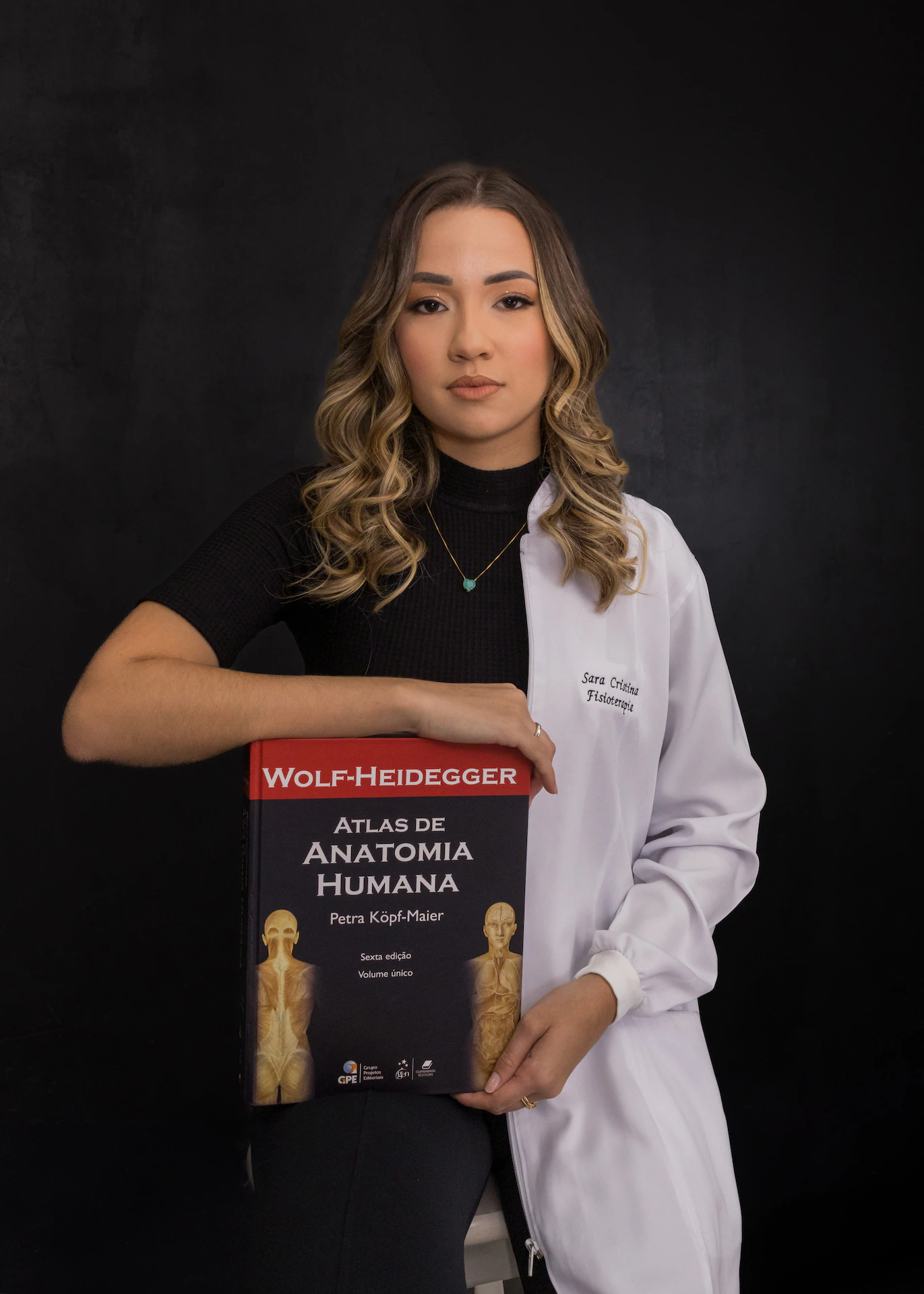 Formanda de jaleco branco segurando o Atlas de Anatomia Humana em ensaio de formatura em Goiânia