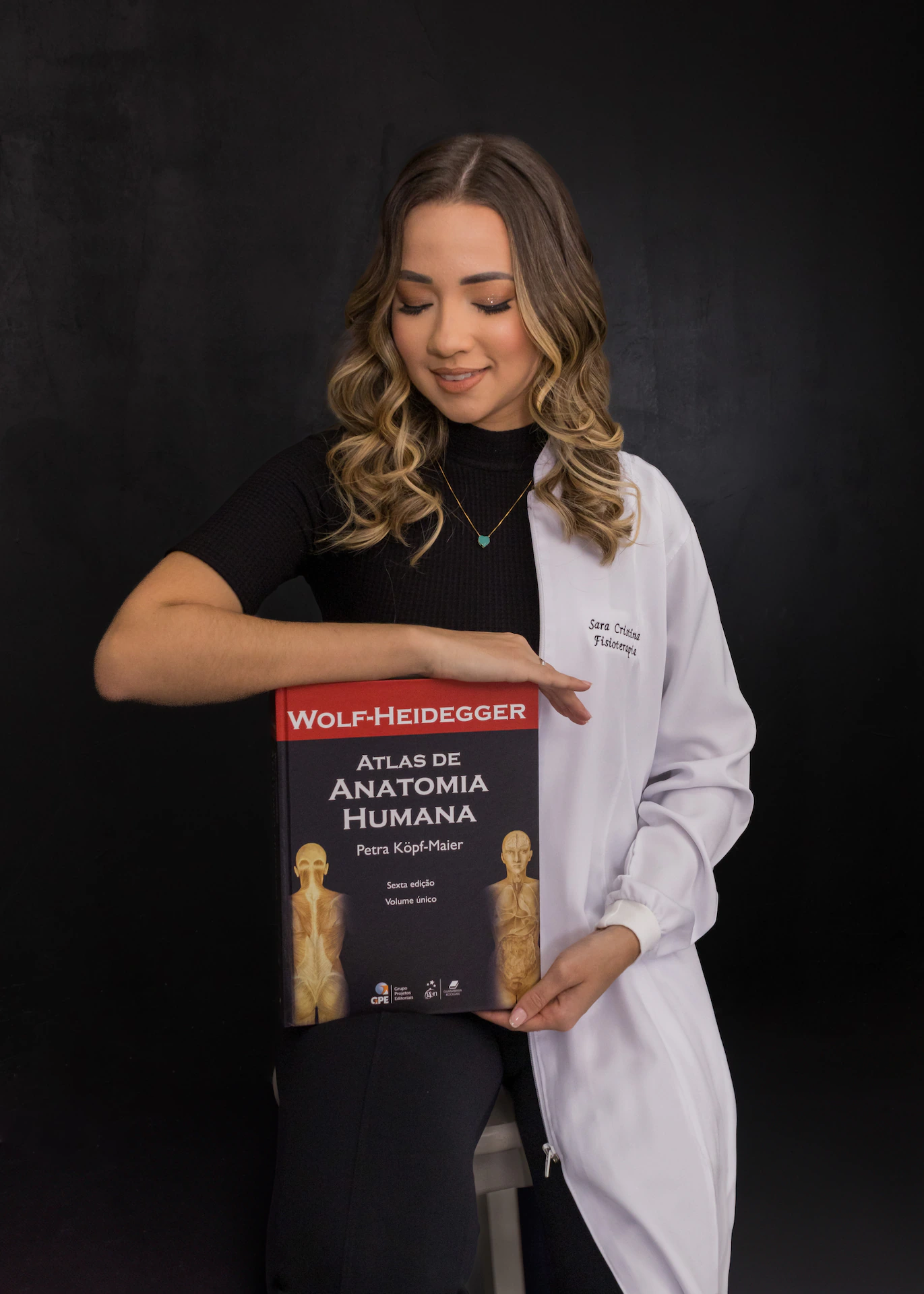 Formanda de jaleco olhando para o livro de anatomia durante o ensaio de formatura