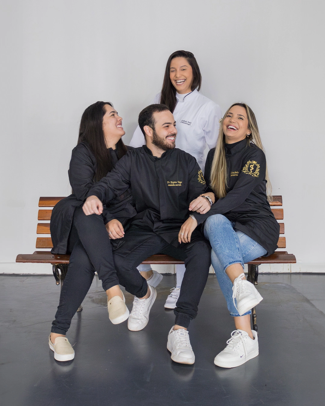 Grupo de formandos de Odontologia sentados num banco, sorrindo, com jaleco preto bordado com o nome
