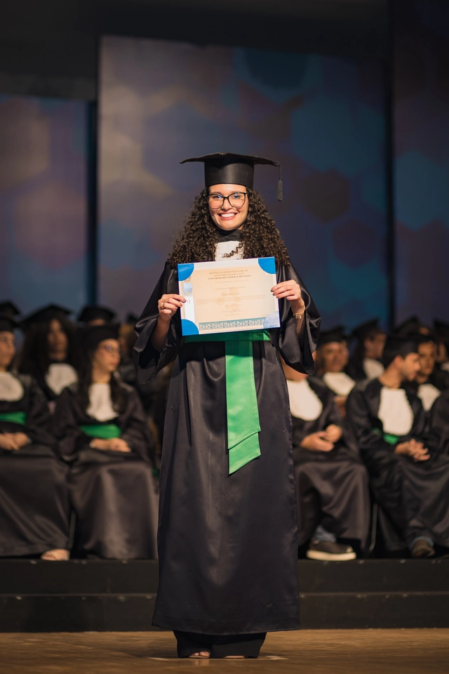 Formanda no palco da colação de grau da UFG, segurando o certificado de Medicina Veterinária