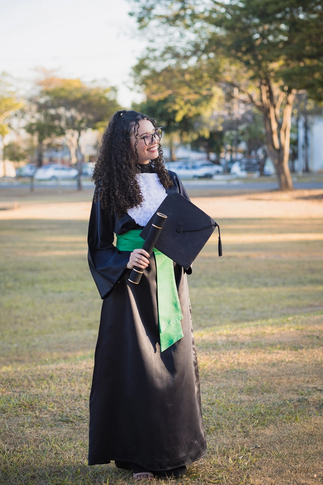 Formanda caminhando pelo campus da UFG com o capelo e o diploma, depois da colação de grau