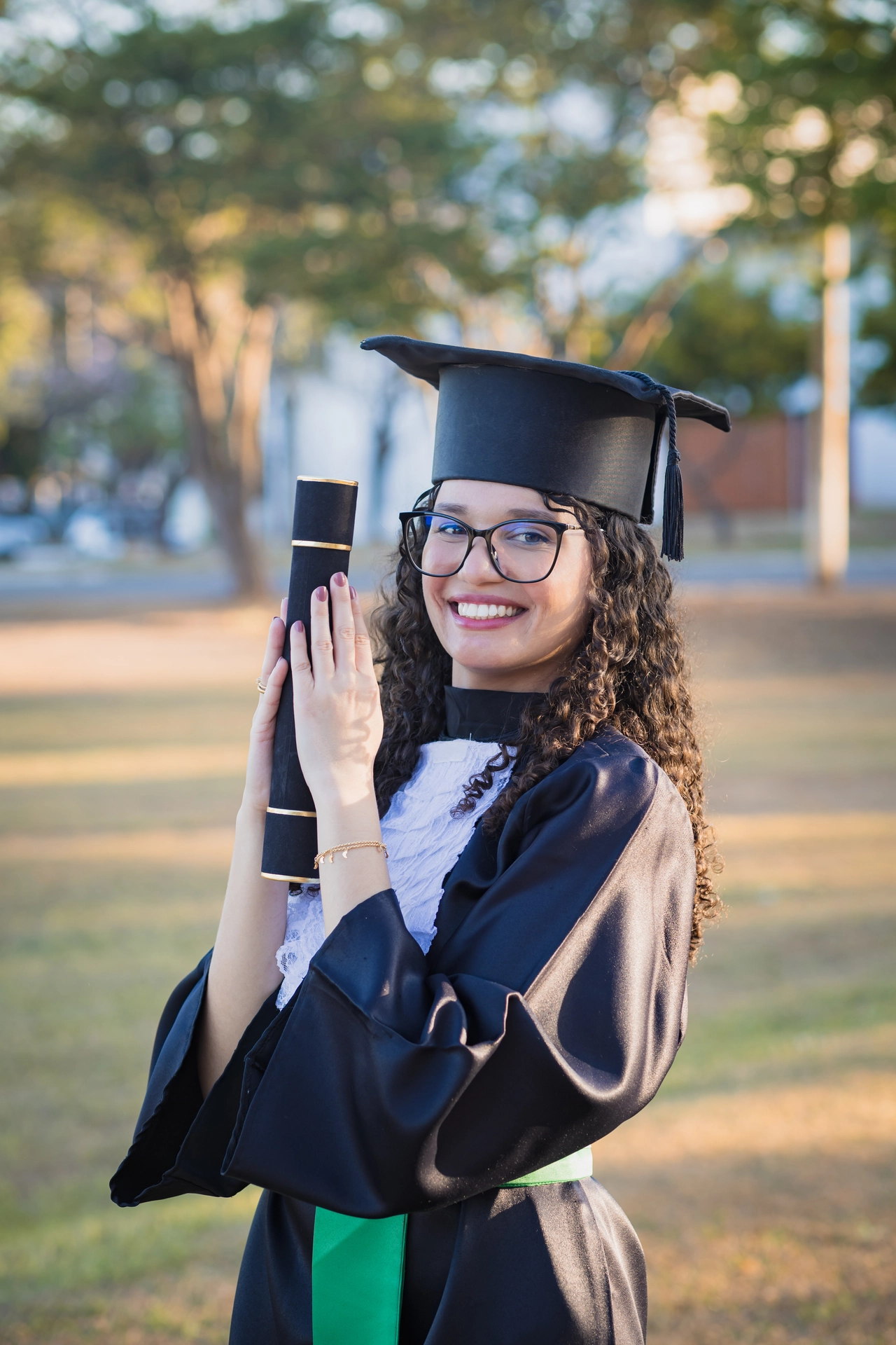 Formanda sorrindo com o diploma próximo ao rosto, no campus