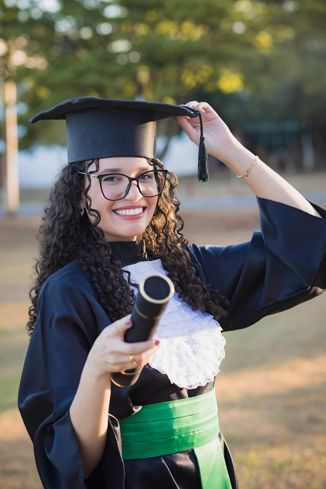 Formanda ajeitando o capelo, com o diploma na mão, no campus da UFG