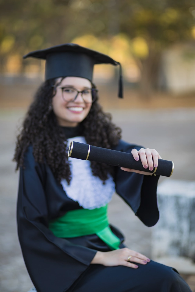 Formanda sentada no campus, com o diploma próximo ao rosto